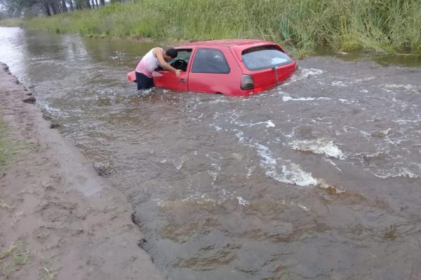 El automovil en medio del agua en un camino que se lo llevo el agua